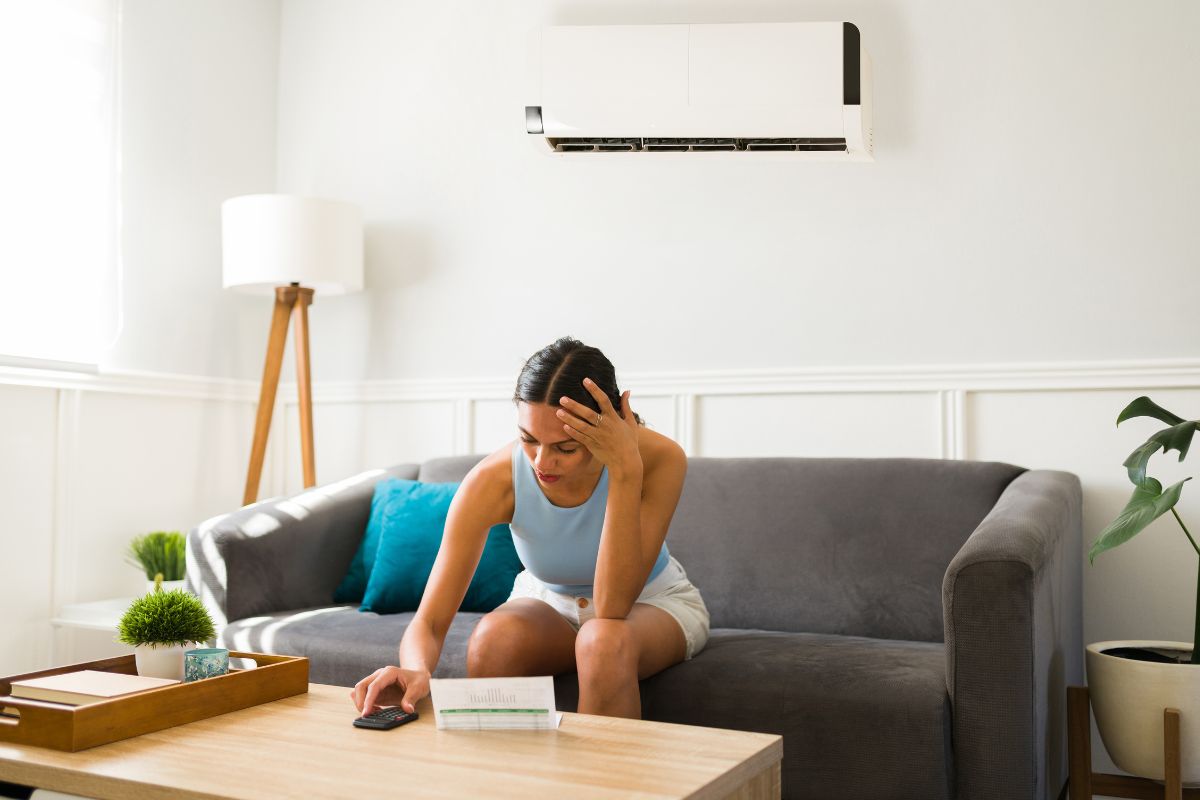 perempuan duduk di ruang tamu dengan ac di atasnya